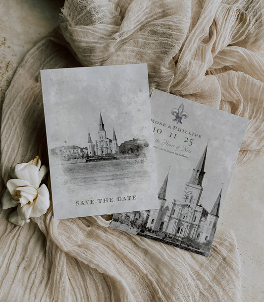 New Orleans save the date featuring a watercolor image of a riverfront view of the St. Louis Cathedral in Jackson Square. A watercolor fleur de lis and your wedding details complete the back of the card.