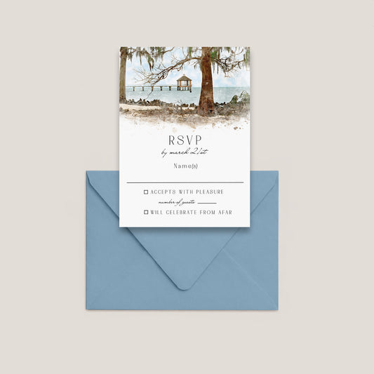 Fontainebleau State Park wedding RSVP card with the beautiful park pier out over of the water of Lake Pontchartrain, beach scene and trees, layered over a dusty blue envelope on a light beige background.