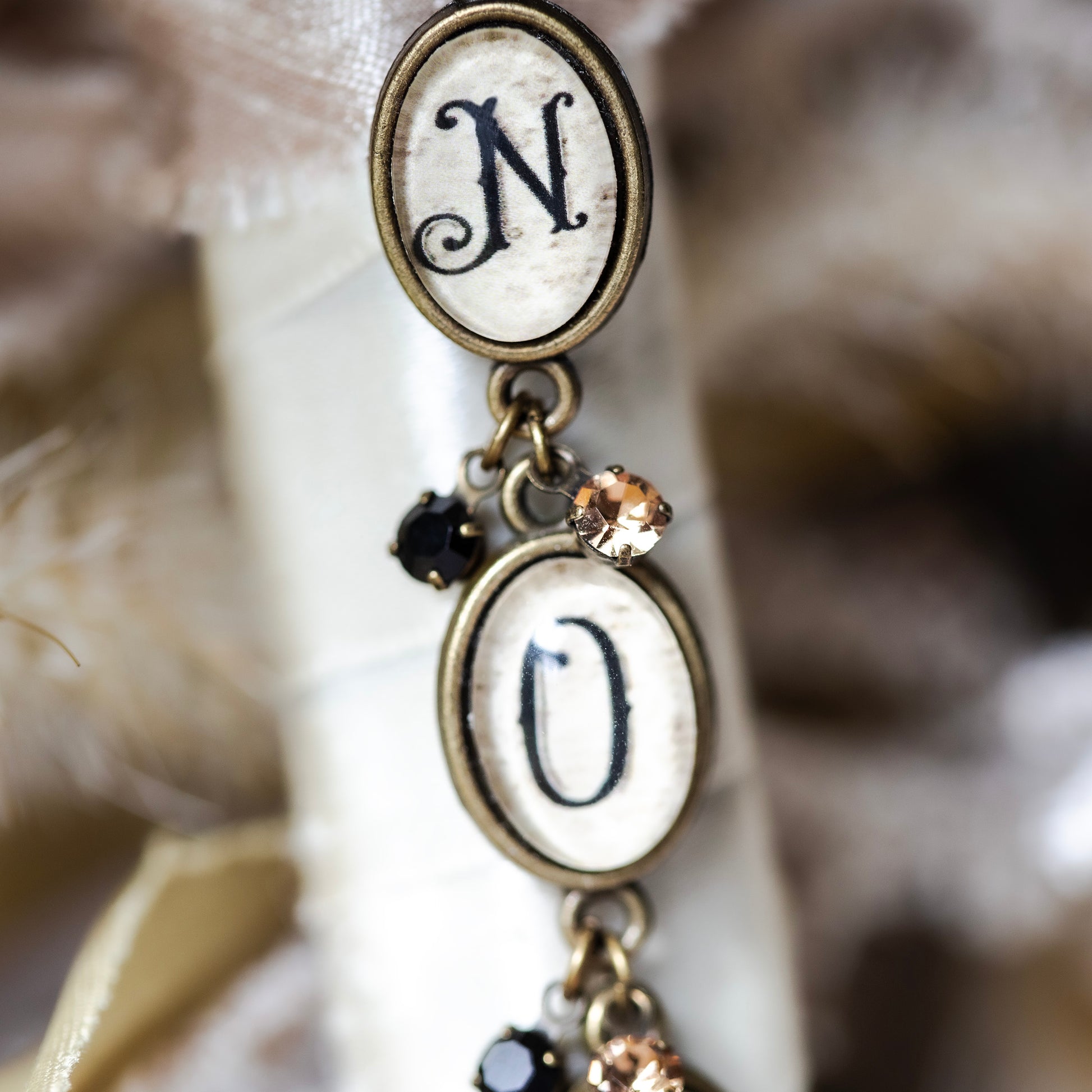 Decorative earrings with 'N' and 'O' charms on a blurred background