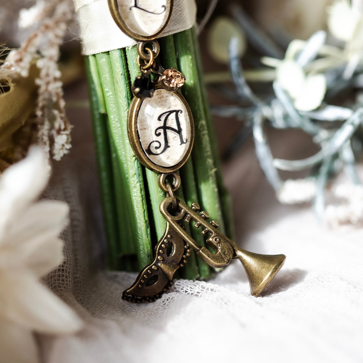 Decorative wedding bouquet charm with letter 'A' charm, a trumpet charm and a Mardi Gras mask charm.