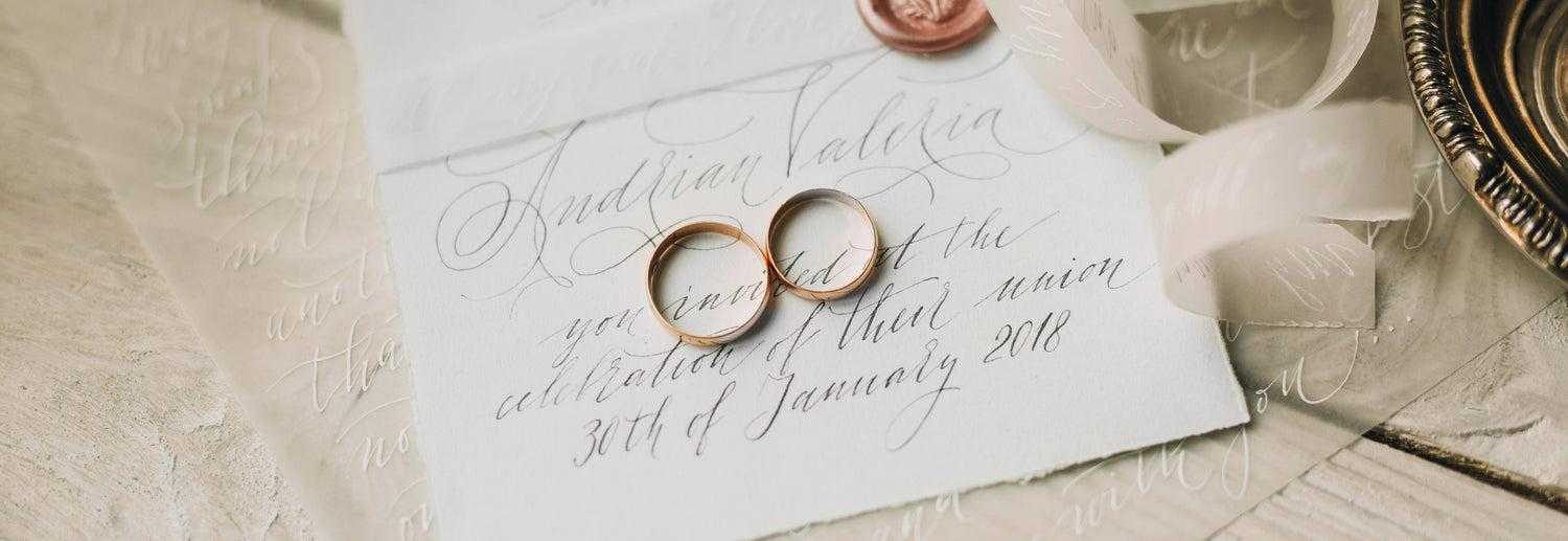Two wedding rings on a vintage wedding invitation with a wax seal and ribbon.